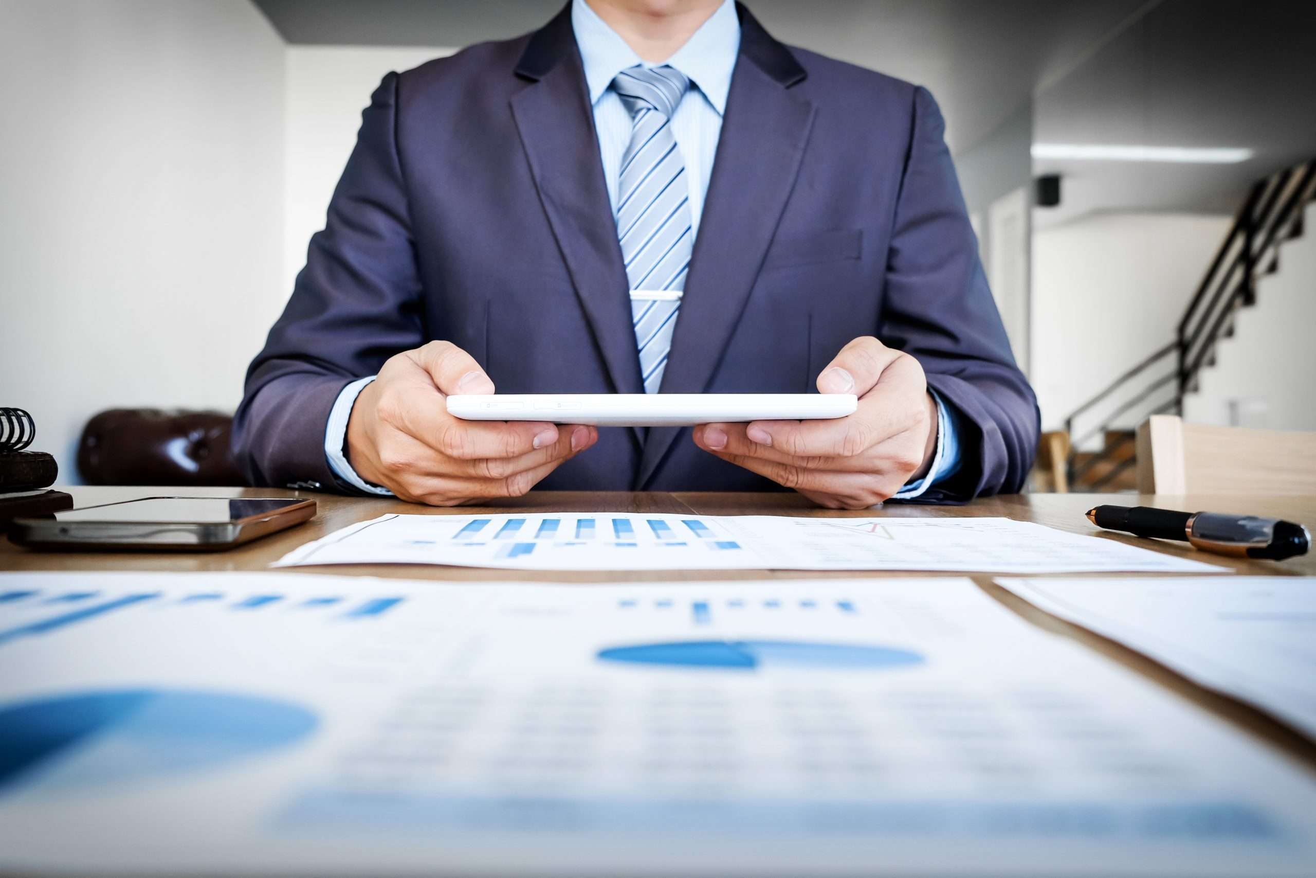 Multitasking. Handsome young man working with touchpad while sitting on the couch in office and financial statistic graph.