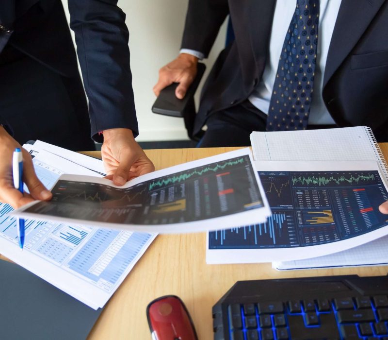 Investor and trader discussing statistic data, holding papers with financial charts and pen. Cropped shot. Broker job or trading concept