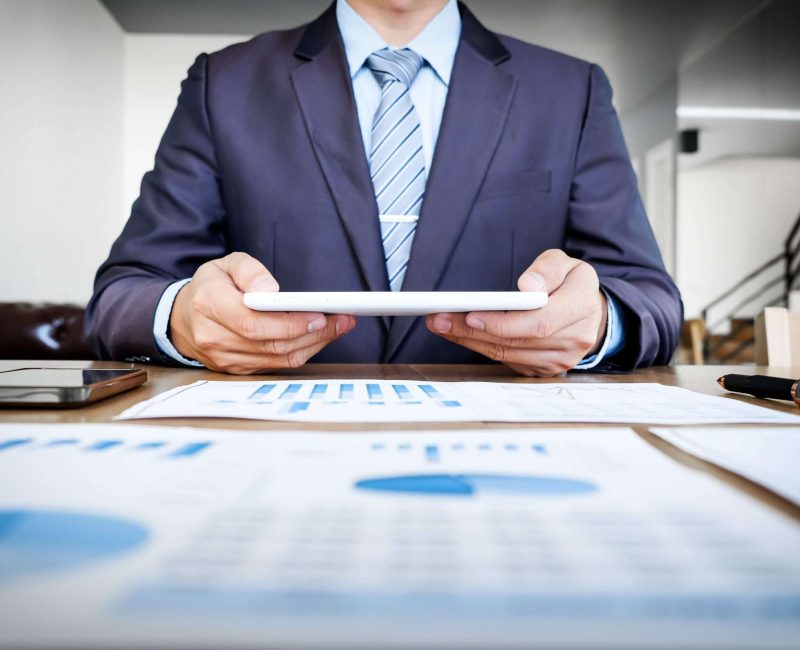 Multitasking. Handsome young man working with touchpad while sitting on the couch in office and financial statistic graph.