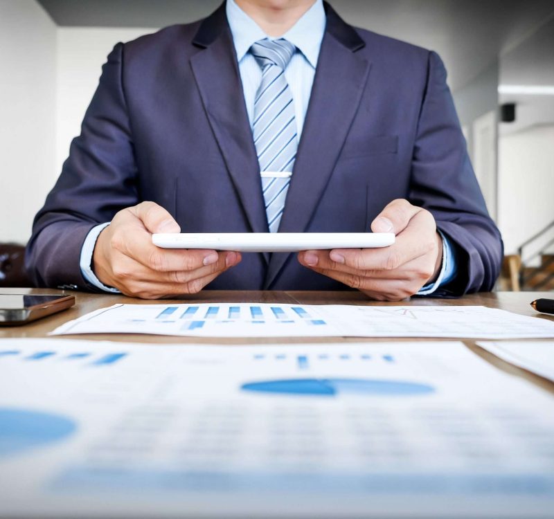 Multitasking. Handsome young man working with touchpad while sitting on the couch in office and financial statistic graph.