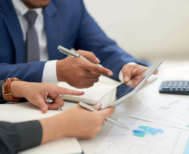 unrecognizable-business-people-sitting-meeting-with-charts-looking-pointing-tablet